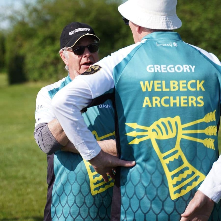 Two men in Welbeck Archers jerseys embracing on the archery field, one named Dave and one named Gregory.
