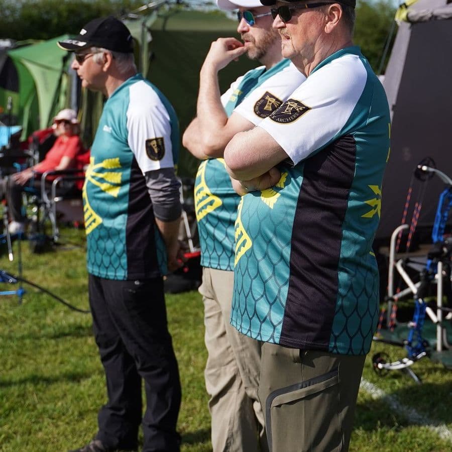 Three archers in Welbeck Archers team shirts standing together, watching a shoot in progress.