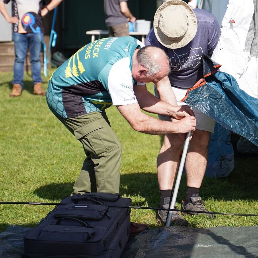 Two Welbeck Archers members helping set up a gazebo and equipment on the grass before a shoot.