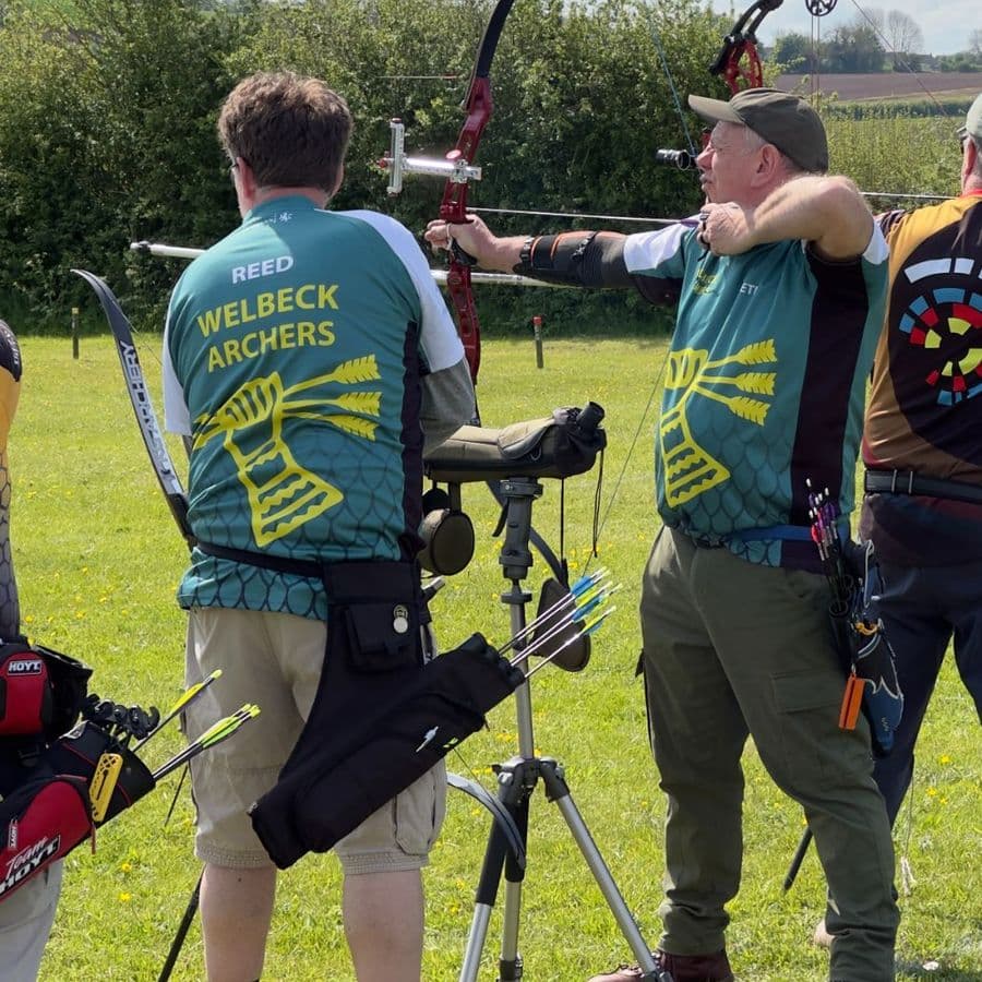 Two archers in Welbeck Archers shirts at full draw side by side on the shooting line.