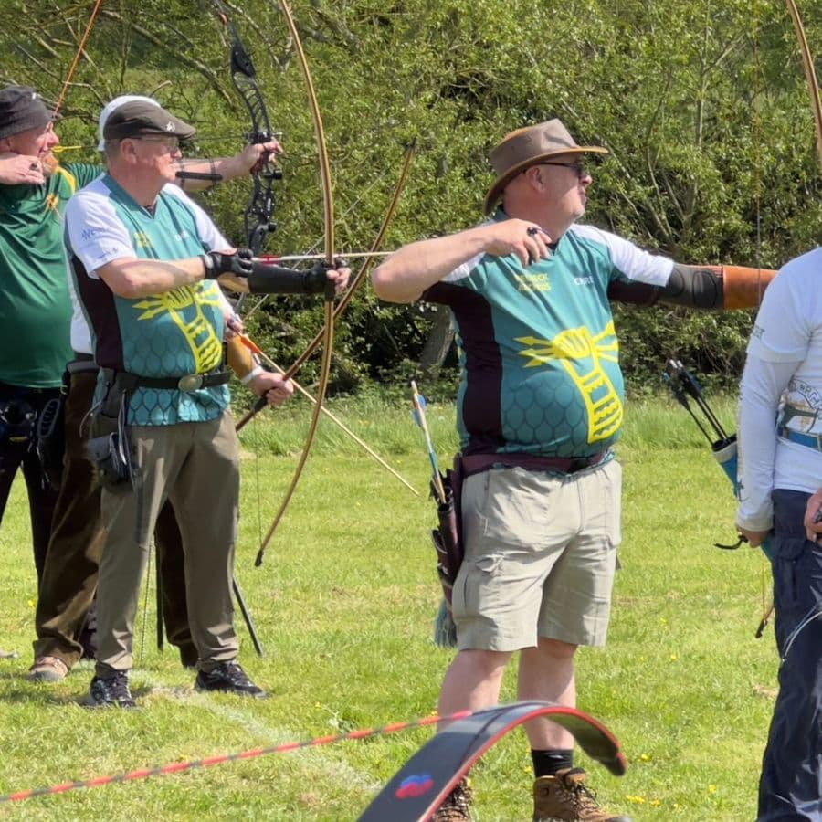 A group of archers in Welbeck Archers team shirts at full draw on the shooting line.