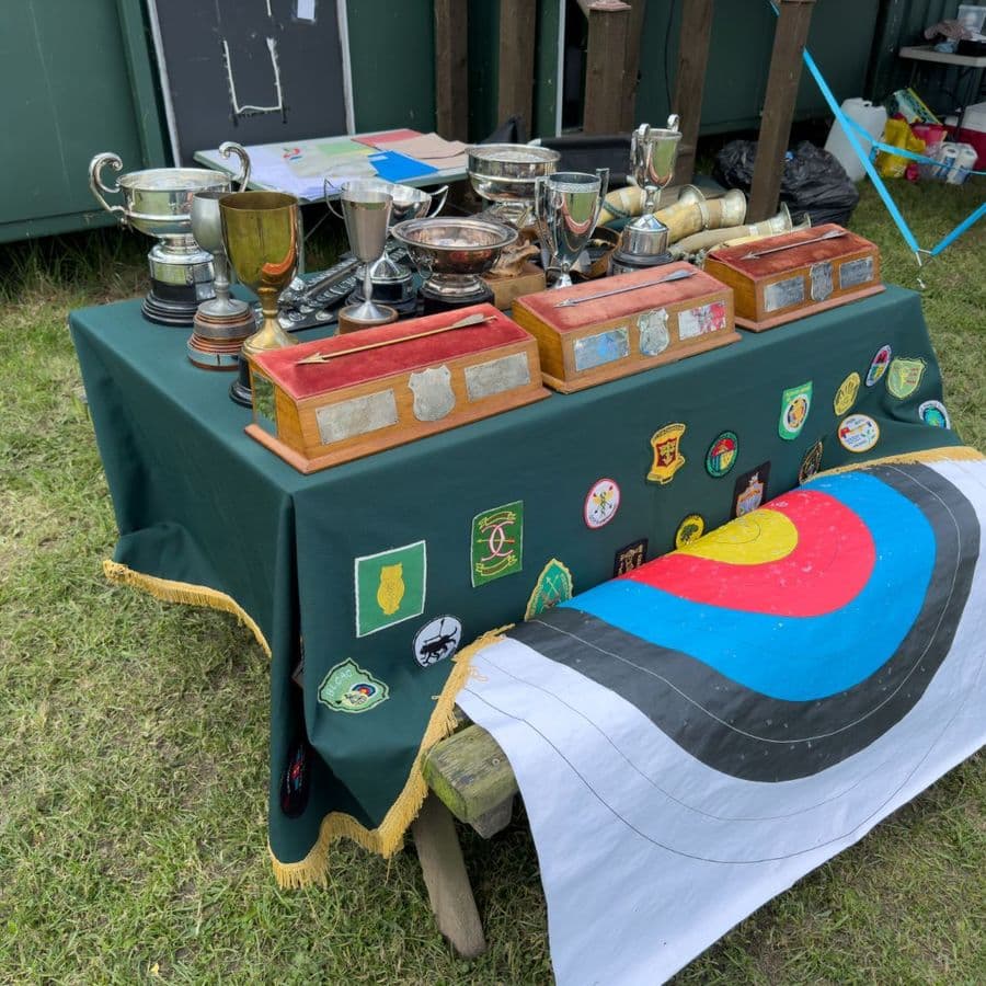 A table of trophies and cups alongside a target face draped with club and county badges.