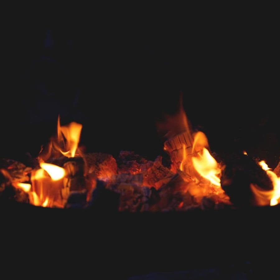 Close-up of glowing embers and flames in a fire pit at night.